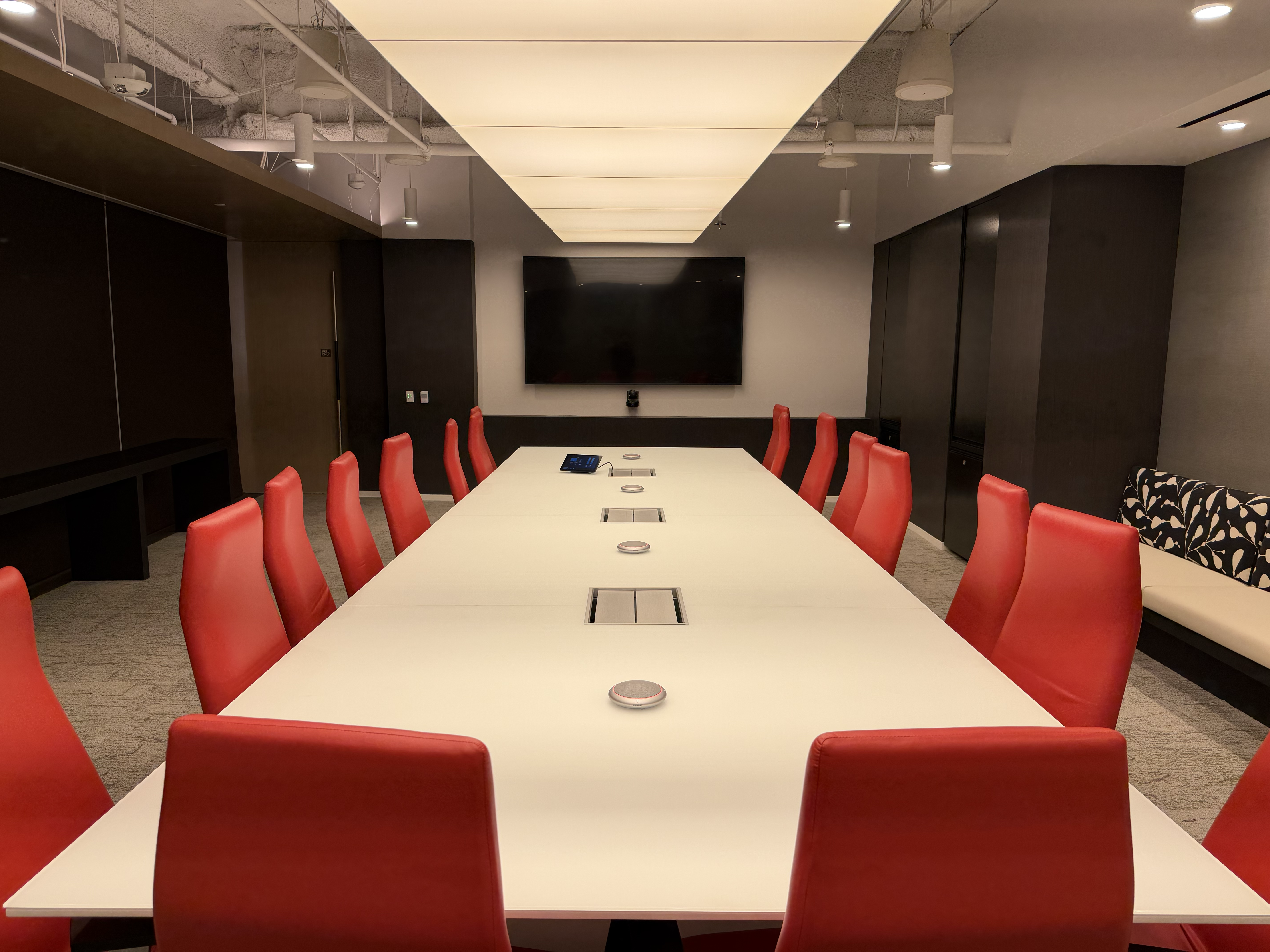 Corporate conference room with a large display, tabletop microphones, and red chairs