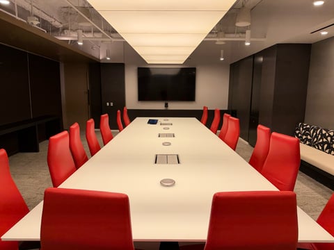 Corporate conference room with a large display, tabletop microphones, and red chairs